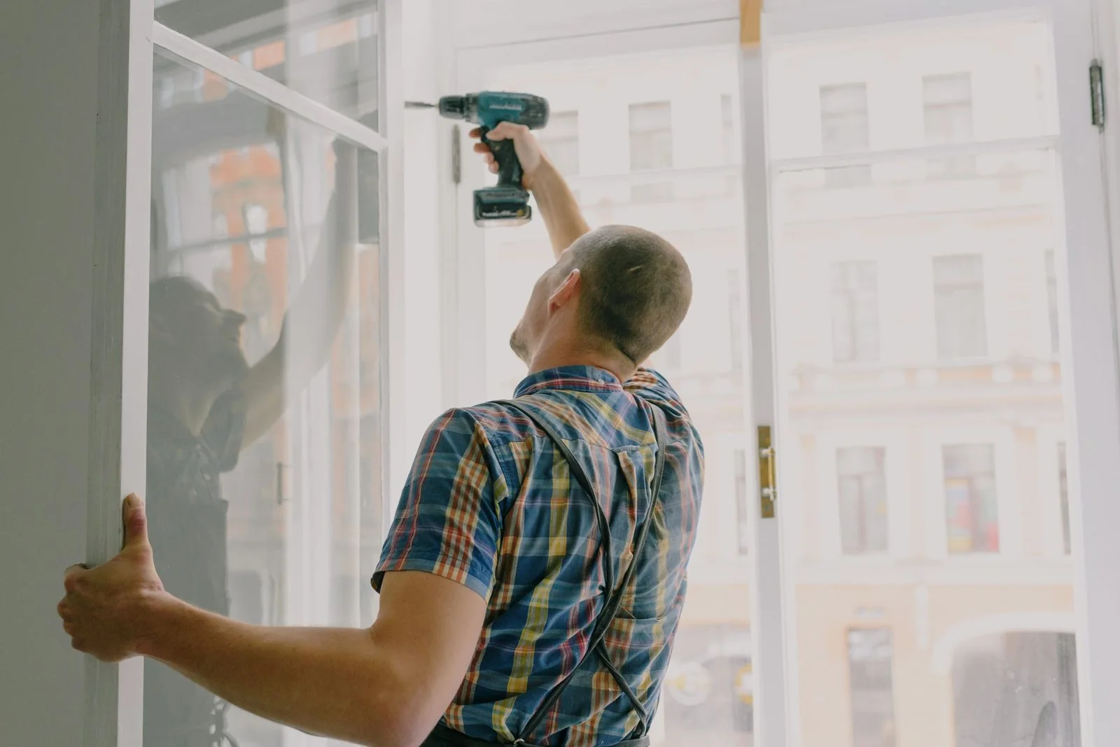 A tradesperson fitting a window frame with a cordless drill